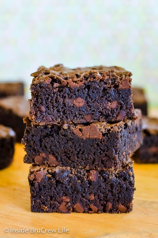 Three homemade chocolate chip brownies stacked on top of each other on a cutting board