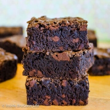 Three homemade chocolate chip brownies stacked on top of each other on a cutting board