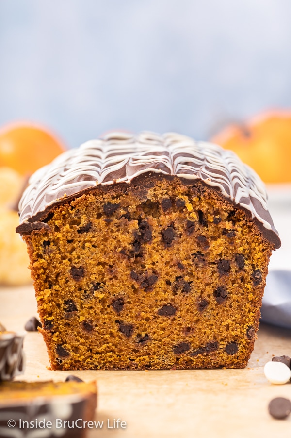 A loaf of pumpkin chocolate chip bread topped with chocolate drizzles on a wooden cutting board.