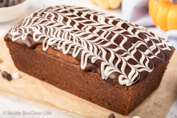 A loaf of pumpkin bread on a tray topped with chocolate and white chocolate drizzles on top.