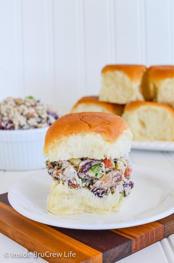 A roll filled with apple cranberry turkey salad sitting on a white plate with more rolls behind it