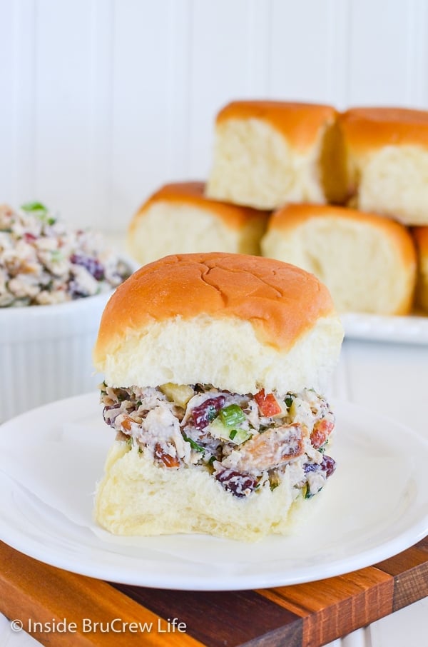 A roll filled with turkey salad on a white plate and more rolls behind it