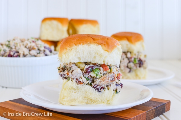 Two plates with a roll filled with turkey salad on each one and a bowl of salad beside it