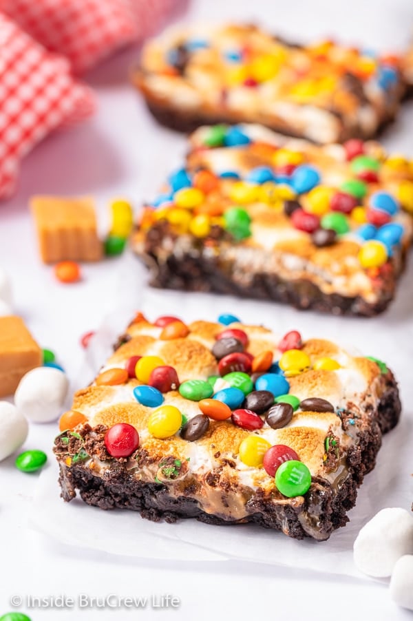 Three caramel marshmallow brownies topped with M&M's on a white board.