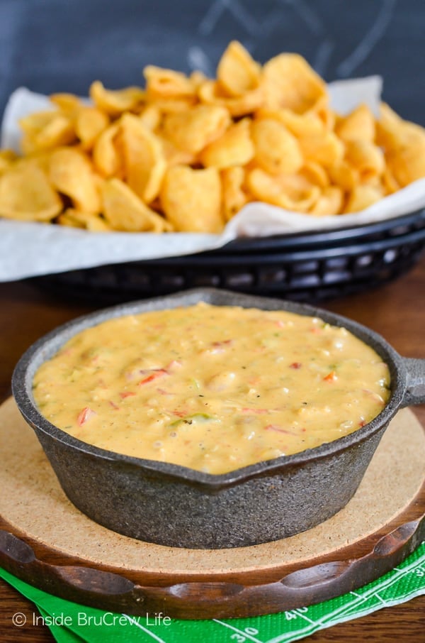 A small cast iron skilled filled with chicken queso dip and a basket of chips behind it.