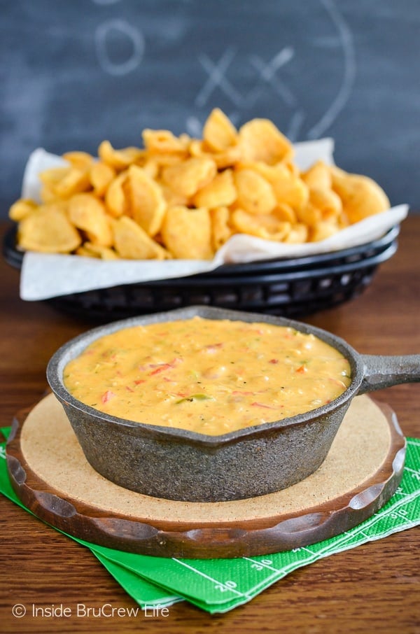 A small cast iron skillet filled with cheesy queso dip with chicken and a basket of chips behind it.