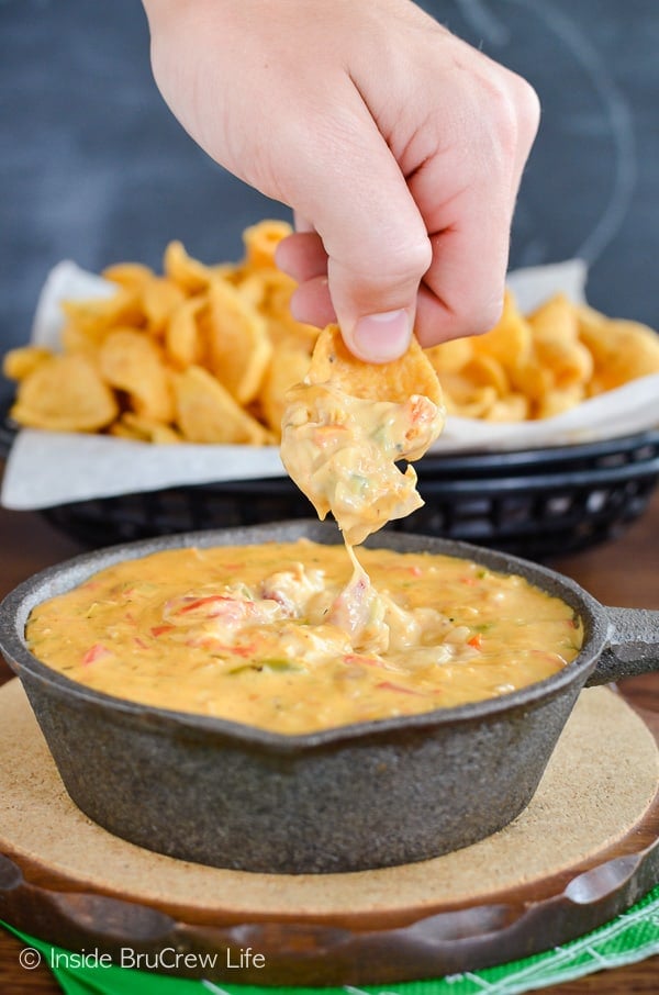 Chicken queso dip in a skillet with a hand lifting a cheesy chip out of it.