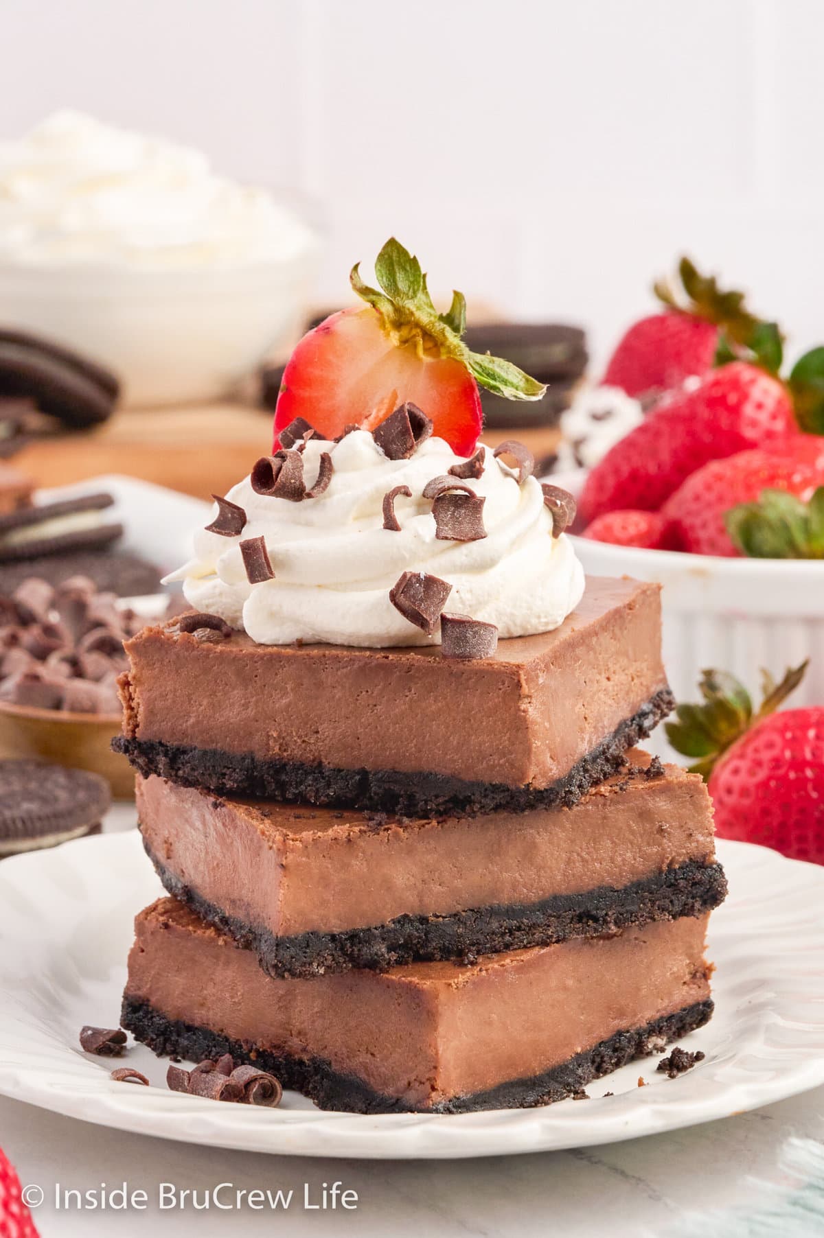 A stack of three chocolate cheesecake bars on a white plate.