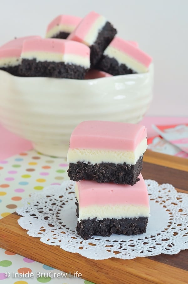 Two squares of neapolitan fudge stacked on top of each other with a white bowl filled with fudge behind it