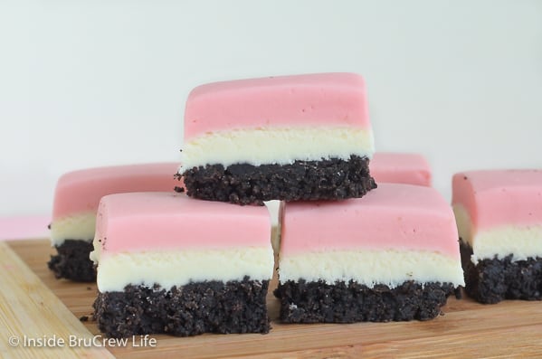 A wooden cutting board with neapolitan fudge squares stacked on it