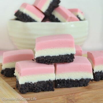 Three squares of neapolitan fudge stacked on top of each other on a wooden board