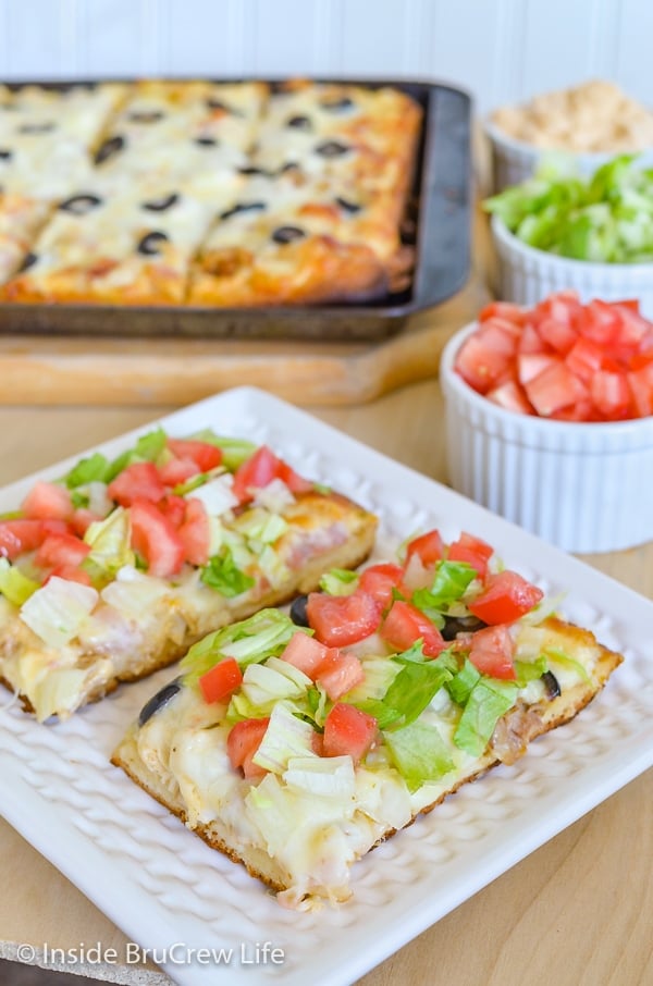 A white plate with two squares of southwest ranch chicken bacon club pizza on it and a sheet pan of pizza behind it