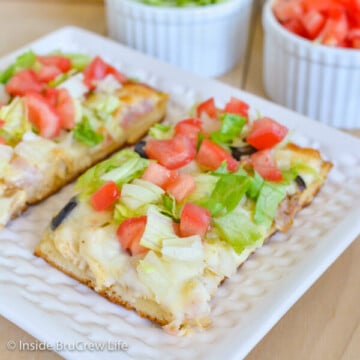 A white plate with two squares of chicken bacon club pizza topped with lettuce and tomatoes