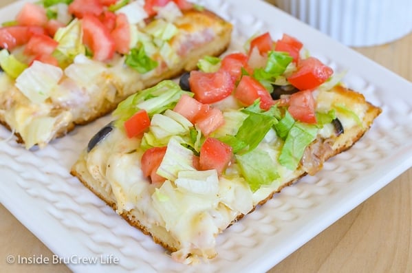 A white plate with two squares of chicken bacon club pizza topped with lettuce and tomatoes on it