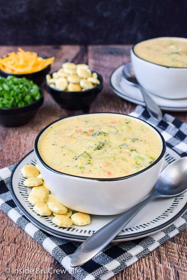 A white bowl with broccoli cheddar soup in it and crackers beside it.