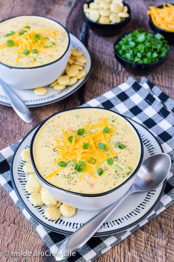 Overhead picture of two bowls of broccoli cheese soup topped with shredded cheese and green onions.