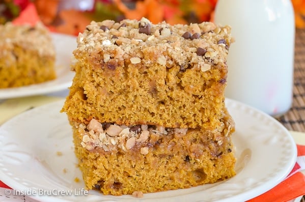 A white plate on an orange napkin with two pieces of pumpkin coffee cake on it