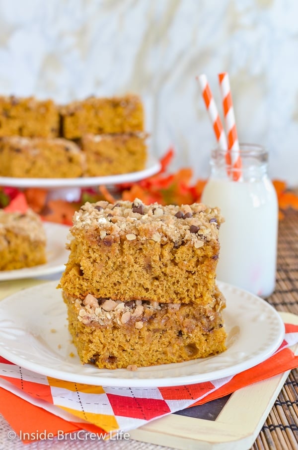 A white plate with two pieces of pumpkin coffee cake on it and a cake plate with more behind it