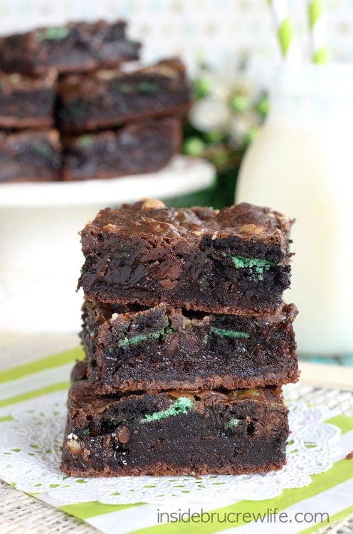 3 brownies stacked together and loaded with green mint cookies with milk in the background.