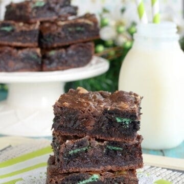 3 brownies stacked together and loaded with green mint cookies with milk in the background.