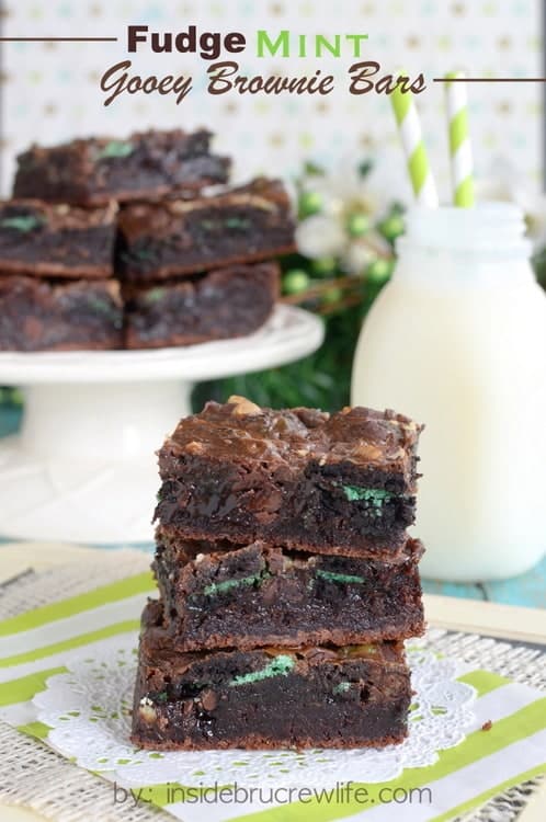 3 brownies stacked together and loaded with green mint cookies with milk in the background. 