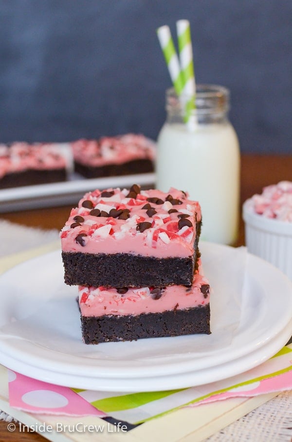 Two Peppermint Chip Brownies stacked together on a white plate with milk in the background.
