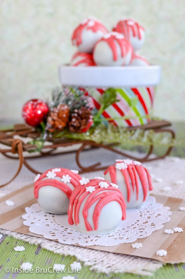 Three peppermint crunch Oreo truffles on a white doily with a bowl of truffles behind them