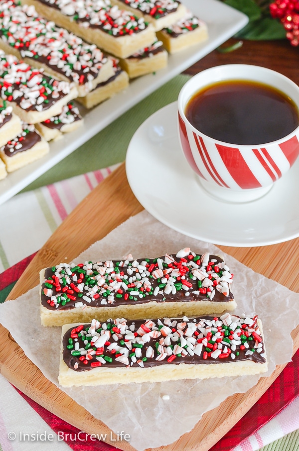 A coffee cup and two shortbread cookies topped with chocolate and candy canes on a wooden board.