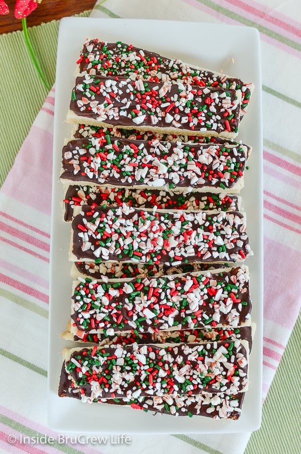 A white plate with a shortbread cookies sticks decorated with dark chocolate, sprinkles, and peppermint bits on it.
