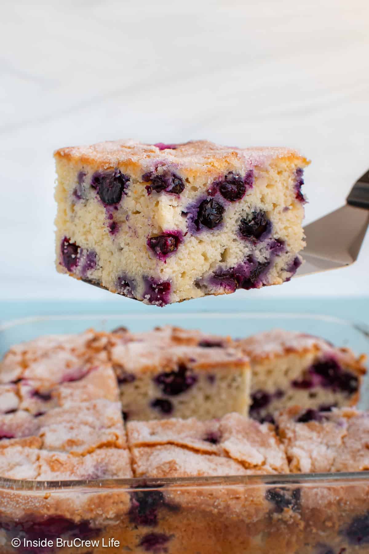 A spatula lifting a piece of blueberry snack cake out of a pan.
