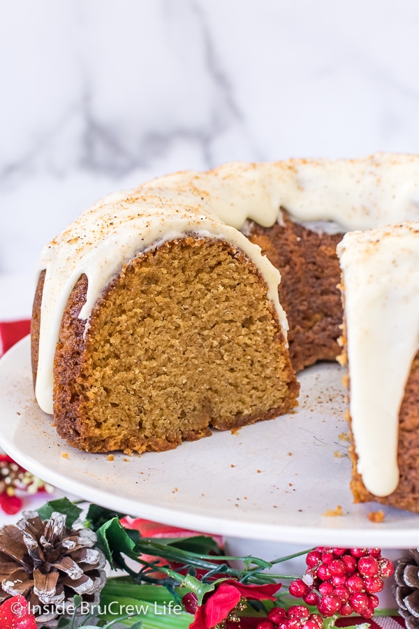 A white cake plate with an eggnog bundt cake on it showing a slice missing