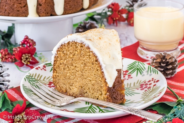 A white plate with a slice of eggnog bundt cake topped with eggnog glaze on it