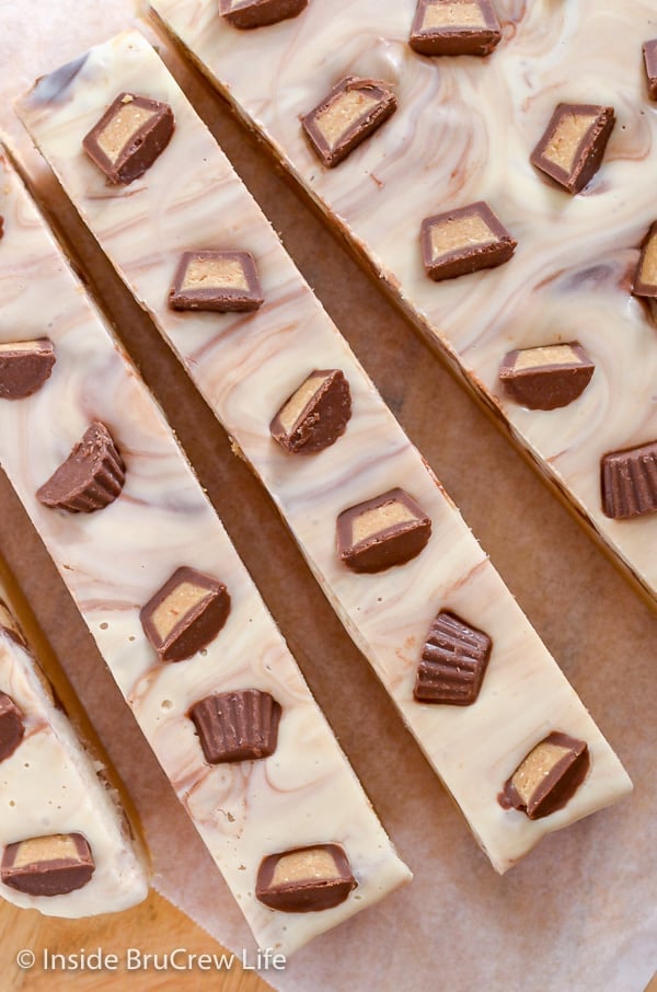 Long strips of White Chocolate Peanut Butter Cup Fudge on a cutting board.
