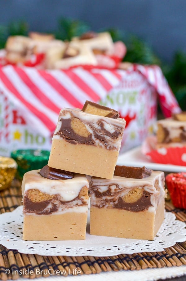 3 pieces of White Chocolate Peanut Butter Cup Fudge with a Christmas tin in the background.