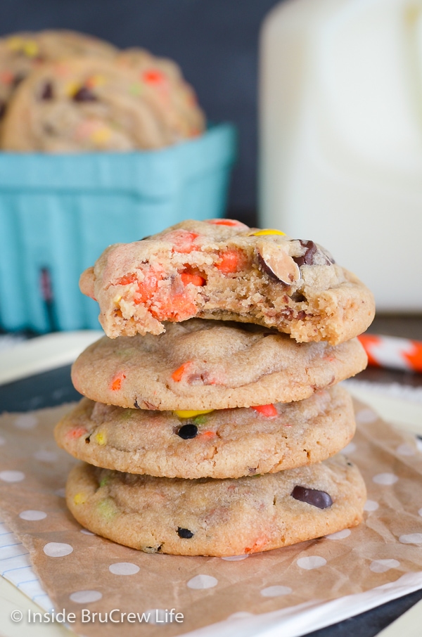 A stack of four peanut butter cookies with Reese's pieces on a piece of brown paper.