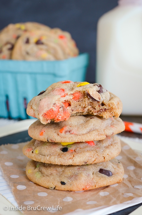 Four peanut butter cookies with Reese's pieces stacked on brown paper.