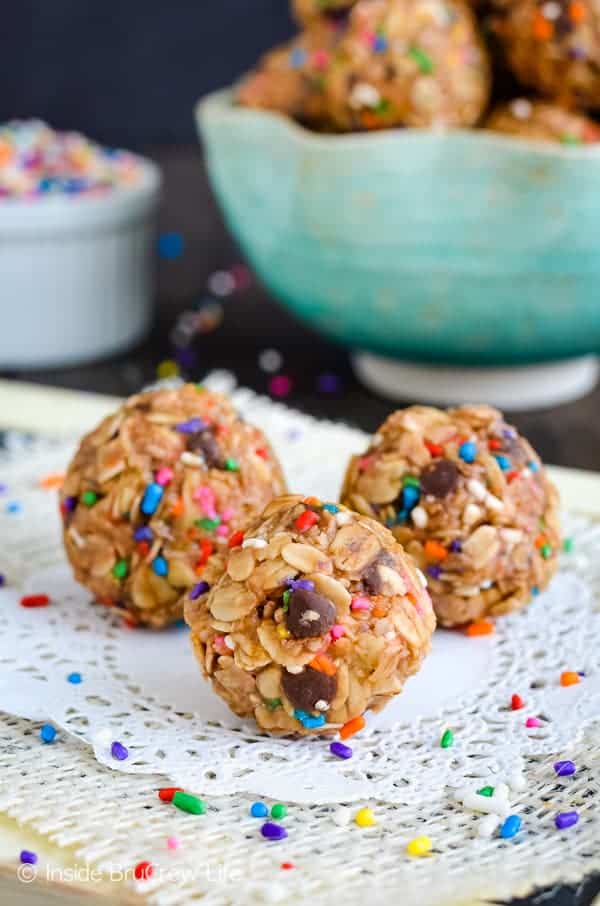 Three peanut butter granola bites on a white doily with a bowl of bites behind them