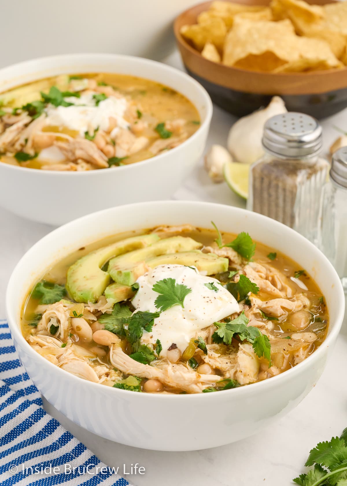 Two white bowls filled with white chicken chili and topped with sour cream and avocados.