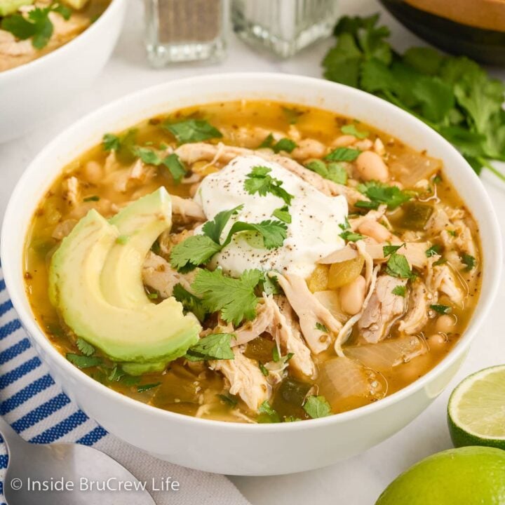 A white bowl filled with chicken chili and topped with sour cream and avocado slices.