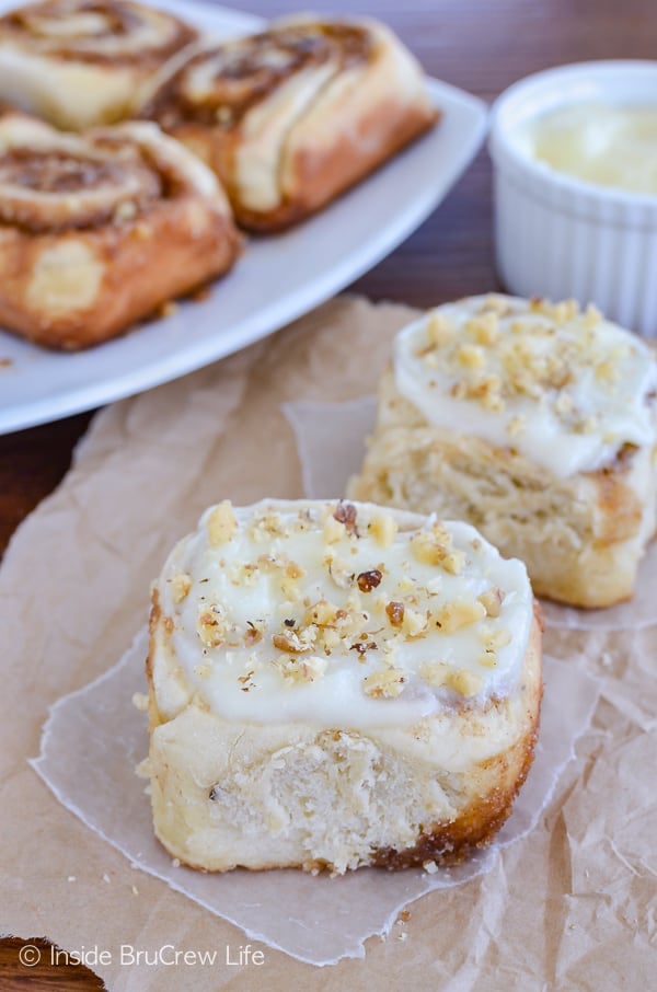 Two banana cinnamon rolls with cream cheese frosting and nuts on a sheet of brown paper.