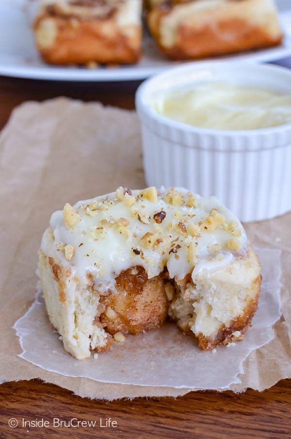A banana nut cinnamon roll with frosting on a piece of parchment with a bite take out of the front.