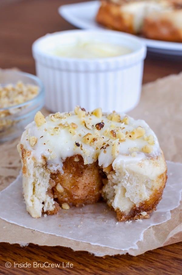 One frosted banana cinnamon roll on a paper with a bite missing showing the cinnamon filling inside.