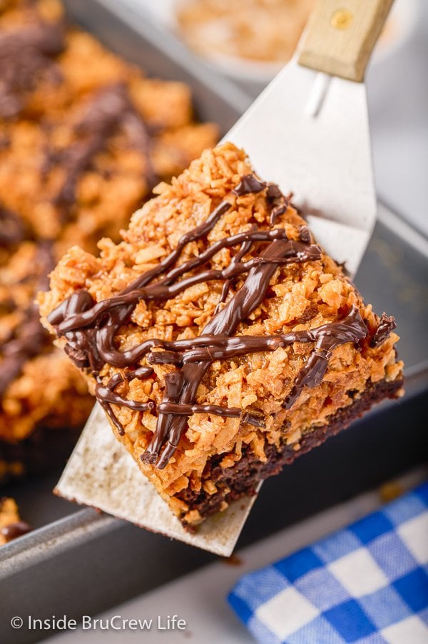 A metal spatula lifting up a brownie topped with a gooey caramel coconut layer.