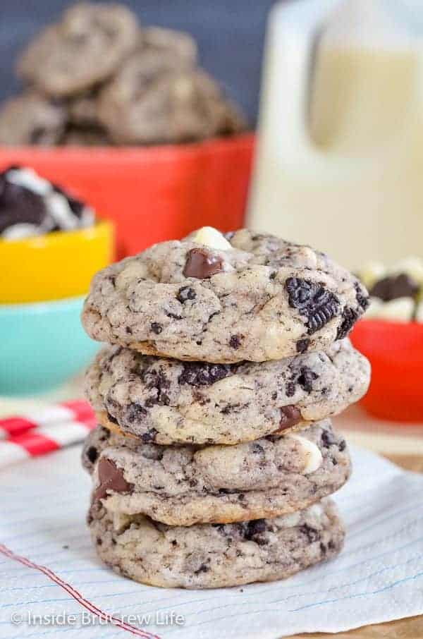 A stack of four chocolate chip cookies and cream cookies on a white napkin with milk behind it