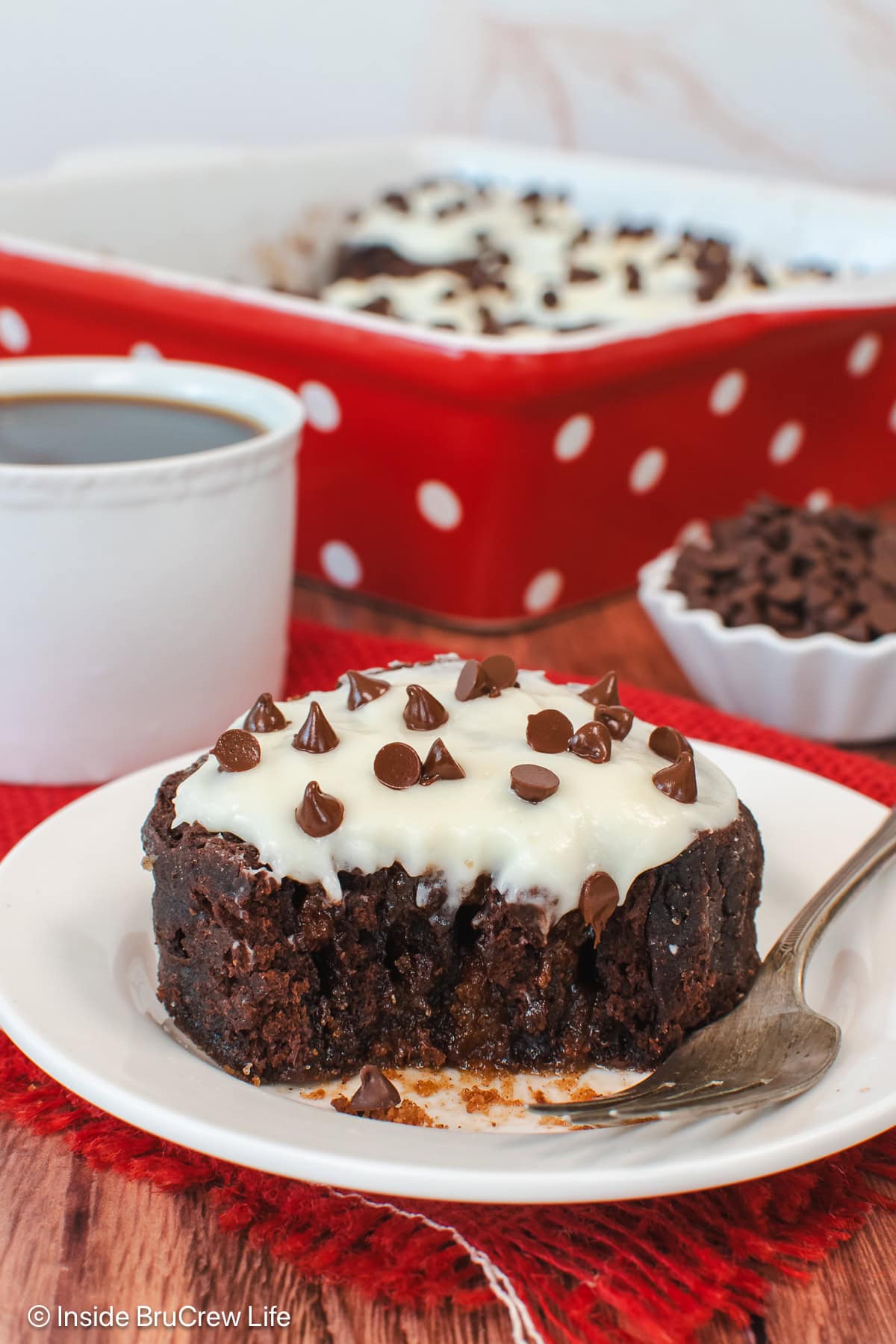 A melty and gooey chocolate cinnamon roll with frosting on a white plate.