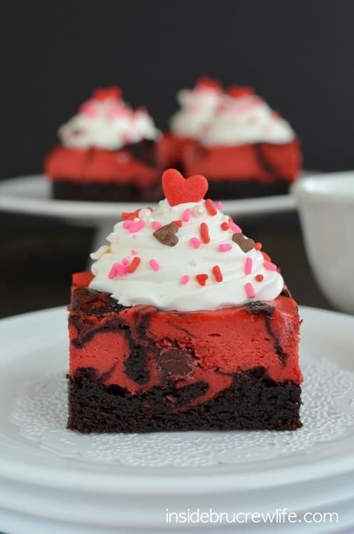 Close up picture of a square of red velvet cheesecake brownies with Cool Whip and sprinkles on a white plate 