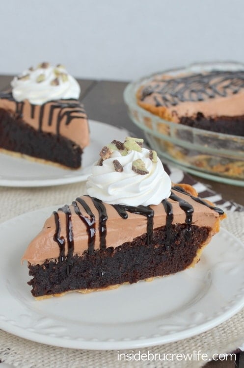 A slice of brownie pie on a white plate topped with a chocolate mint no bake cheesecake.