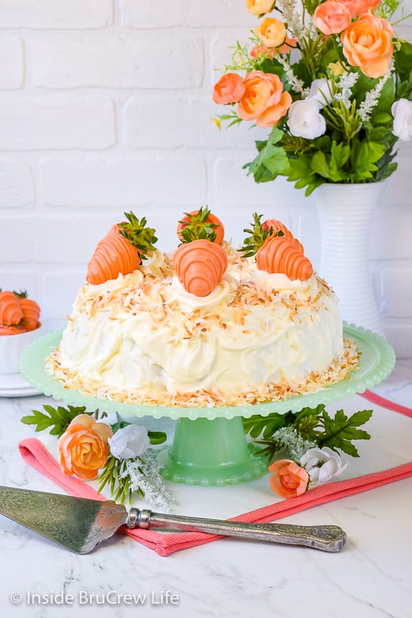 A full size bundt cake topped with cream cheese frosting and toasted coconut on a light green cake plate.