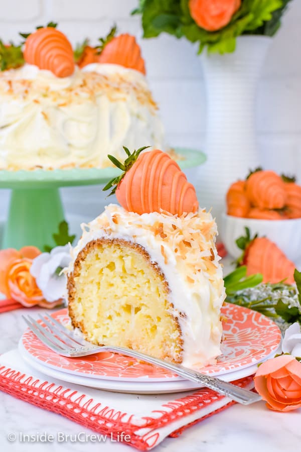 Coconut bundt cake topped with coconut frosting and toasted coconut on a peach colored plate.