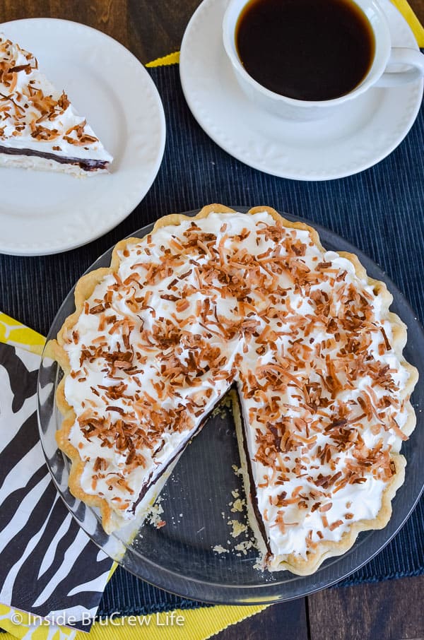 Overhead picture of a whole coconut cream chocolate pie with one slice out on a white plate behind it